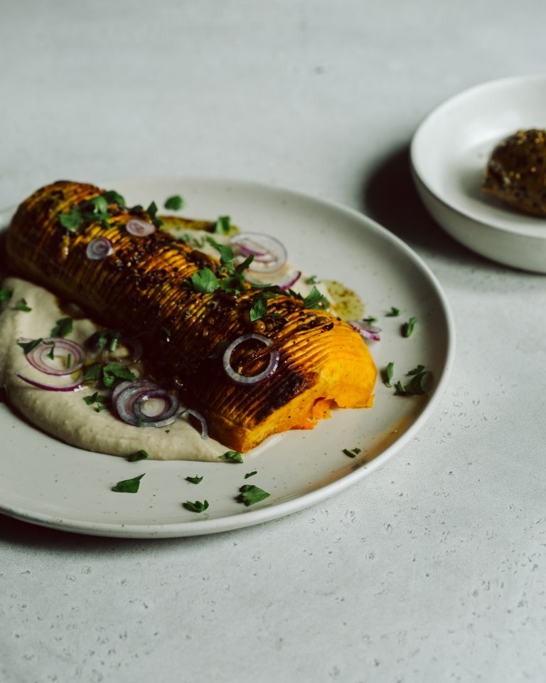Butternut Kürbis Rezept: knusprig gebackener Kürbis auf cremiger Bohnencreme, serviert mit roten Zwiebeln und frischen Kräutern – perfektes veganes Herbstgericht.