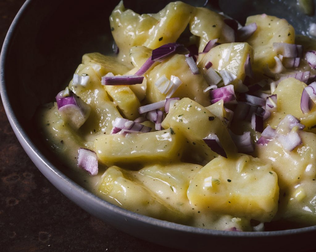 Veganer Kartoffelsalat mit roten Zwiebeln in Schüssel, serviert als klassische Grillbeilage