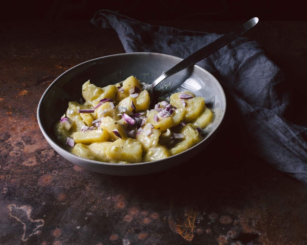 Veganer Kartoffelsalat mit roten Zwiebeln in Schüssel, serviert als klassische Grillbeilage