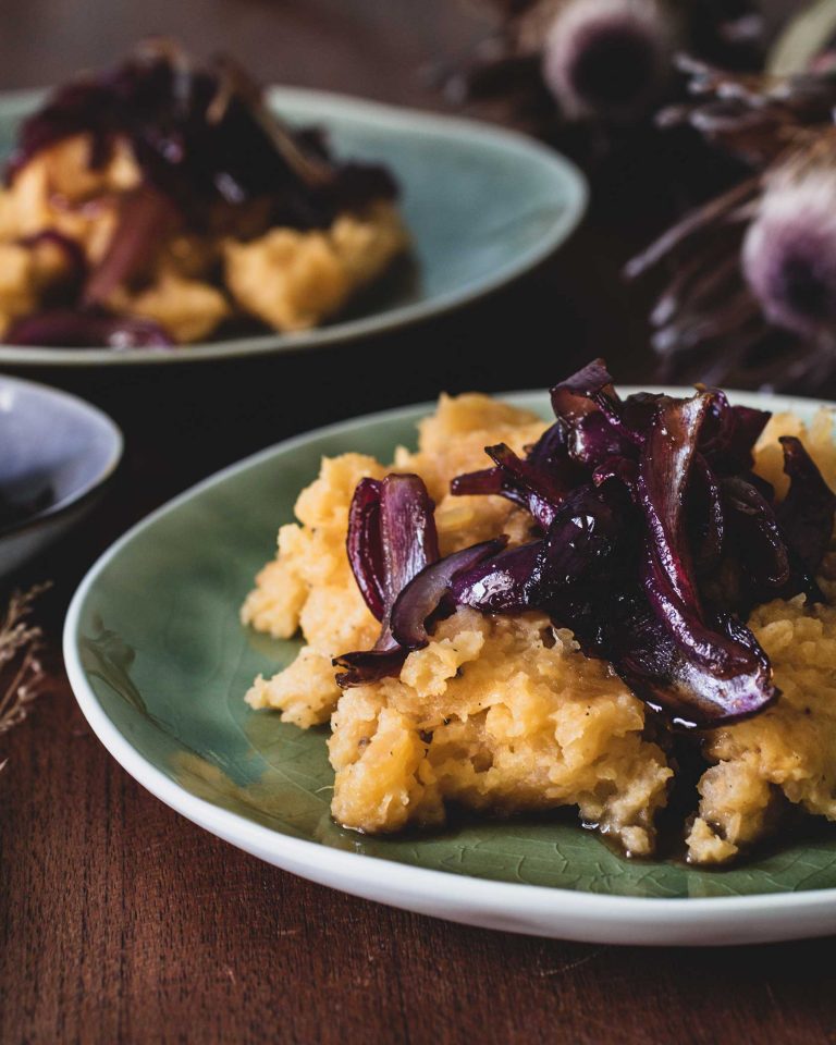 Cremiger Steckrübenstampf auf einem Teller, getoppt mit glänzend karamellisierten roten Zwiebeln