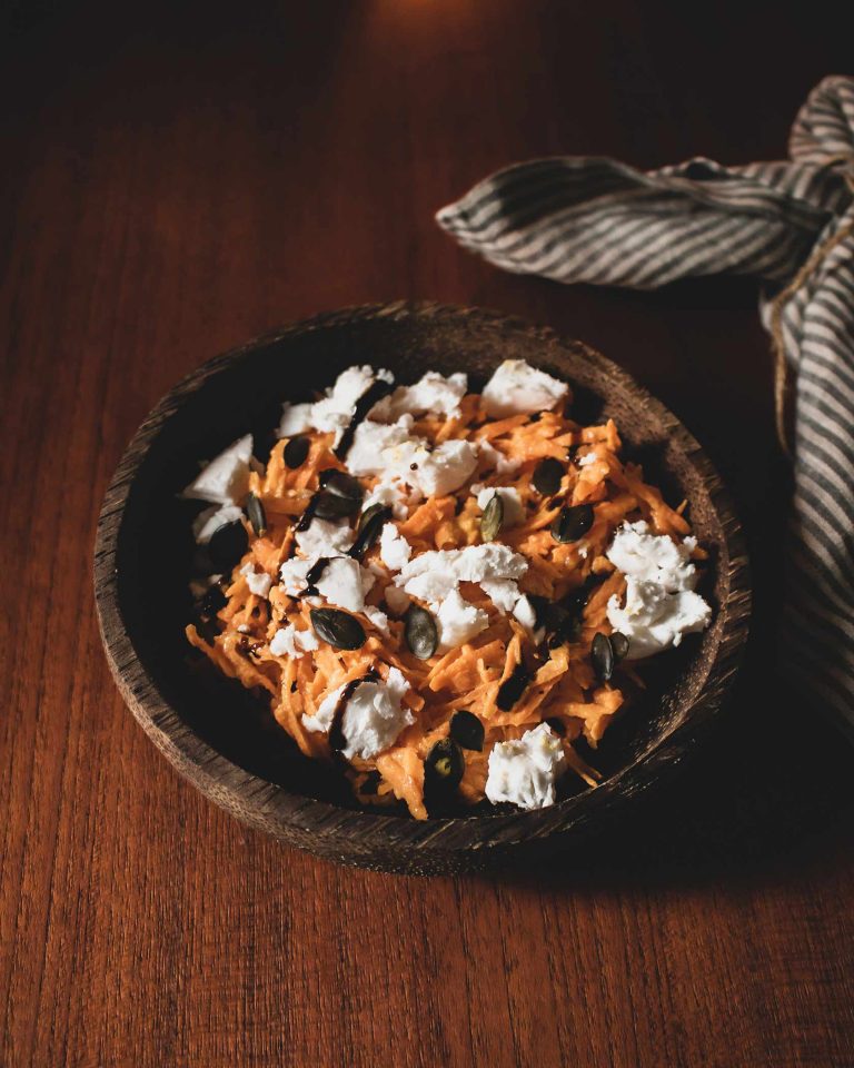 Frischer Karottensalat mit veganem Feta, Kürbiskernen und Balsamicocreme auf einem Teller angerichtet.