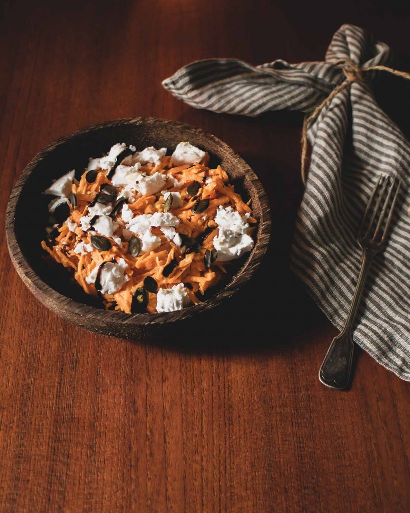 Frischer Karottensalat mit veganem Feta, Kürbiskernen und Balsamicocreme auf einem Teller angerichtet.