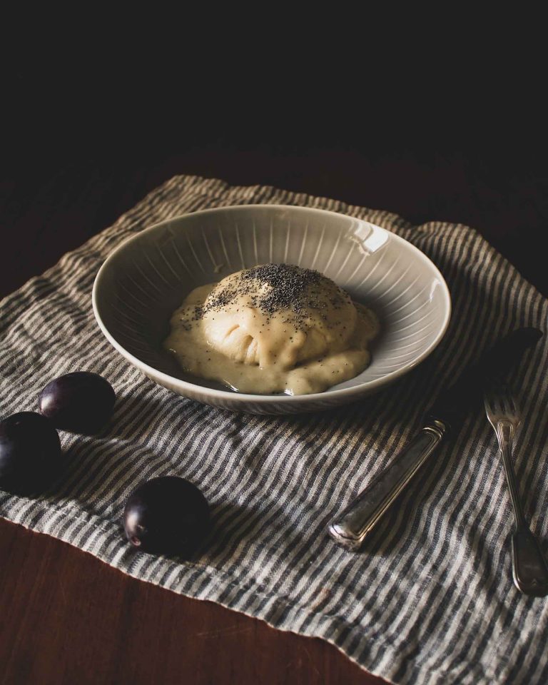 Vegane Germknödel mit Vanillesauce und Mohn bestreut, auf einem Teller serviert.