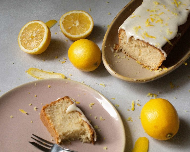 Veganer Zitronenkuchen mit Zuckerguss und Zitronenscheiben auf heller Platte