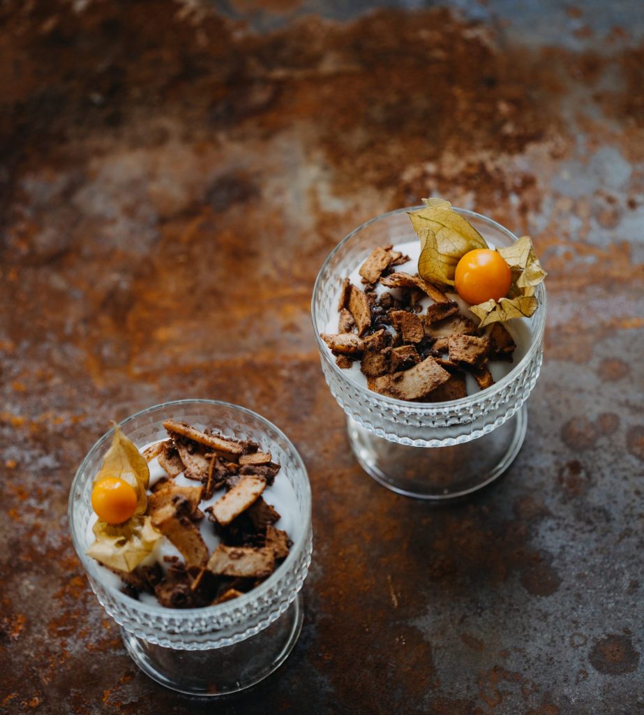 eganes Dessert aus Greek-Style-Joghurt mit karamellisierten Kokosflakes und Physalis im Glas serviert