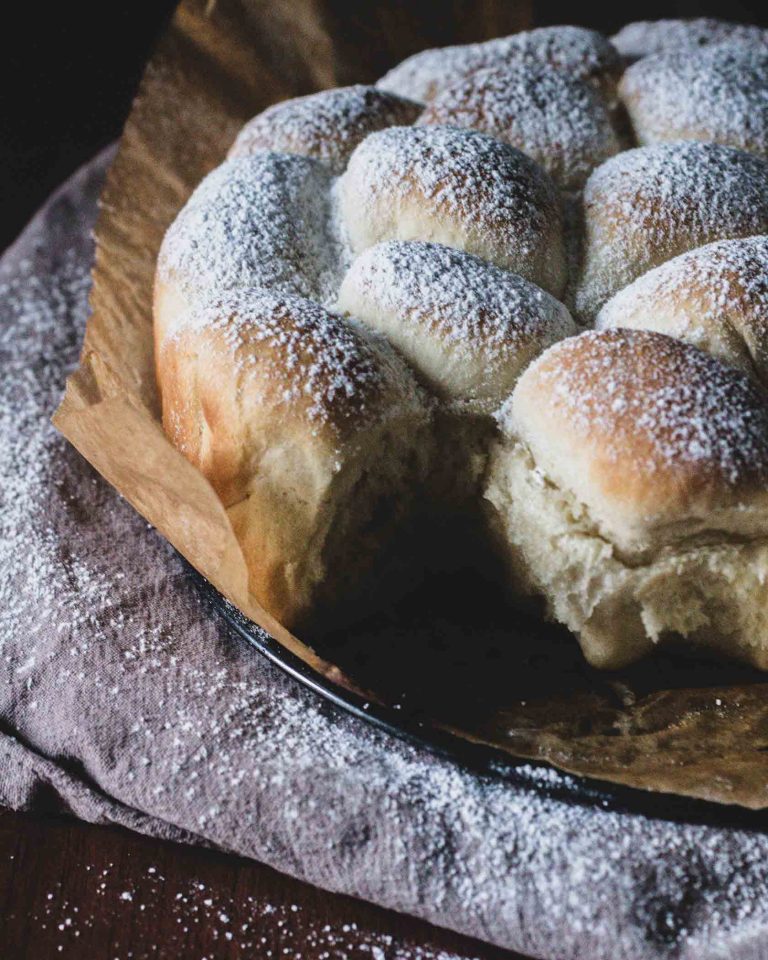 Goldbraune vegane Buchteln dicht aneinander gebacken und mit Puderzucker bestäubt