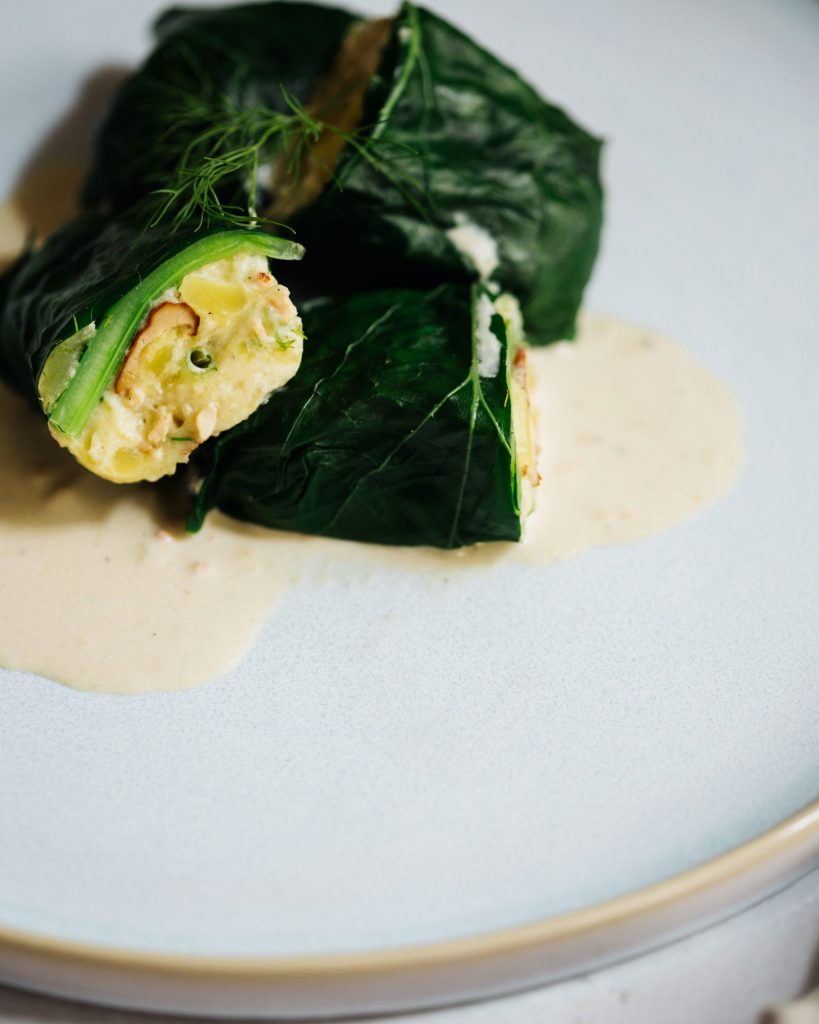 Gefüllte Kohlrabiblätter mit Kartoffel-Räuchertofu-Füllung und cremiger Dillsoße auf einem Teller